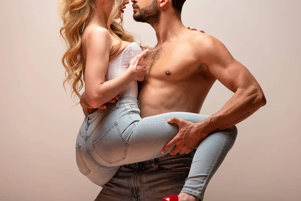 Обрезанный вид мускулистого мужчины касающегося ноги сексуальной женщины в джинсах, изолированных на сером — стоковое фото