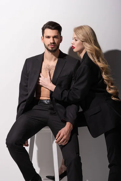 Beautiful woman with red lips touching muscular man sitting on white — Stock Photo