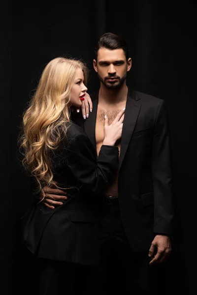 Atractivo rizado mujer tocando guapo hombre aislado en negro - foto de stock