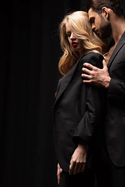 Красивий чоловік торкається красивої жінки в костюмі ізольовано на чорному — стокове фото