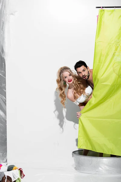 Feliz pin up mulher e homem surpreso cobrindo com cortina de chuveiro no branco — Fotografia de Stock