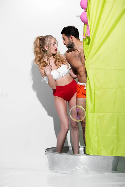 Shocked pin up woman and bearded man looking at each other near shower curtain on white — Stock Photo