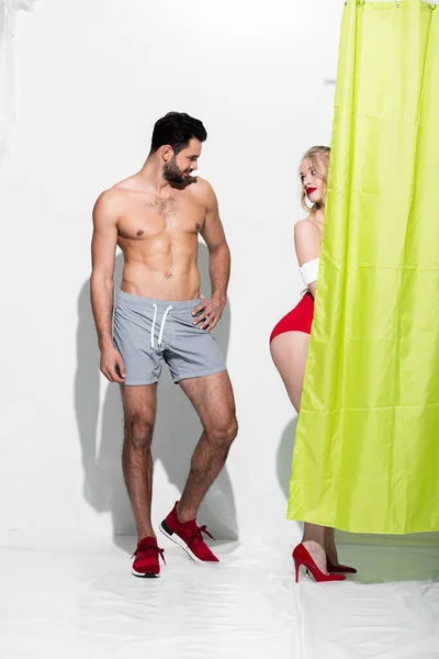 Happy man looking at buttocks of seductive pin up girl standing near shower curtain on white — Stock Photo