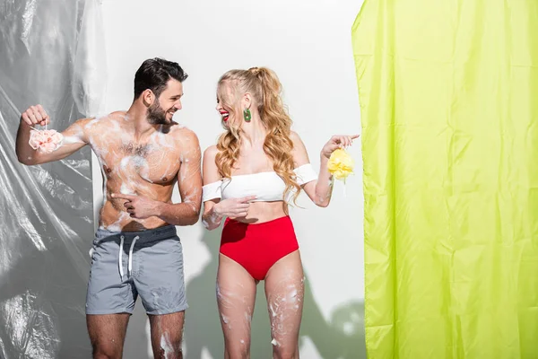 Сексуальная девушка с мокрой губкой и мылом рядом с мужчиной без рубашки на белом — стоковое фото
