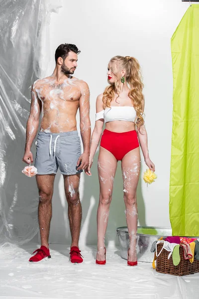 Sexy pin up girl holding wet sponge with soap near shirtless man on white — Stock Photo