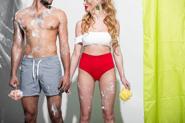 Сексуальная девушка с мокрой губкой и мылом рядом с мужчиной без рубашки на белом — стоковое фото