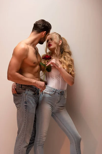 Hemdloser Mann mit Rose und Blick auf attraktives Mädchen auf grau — Stockfoto