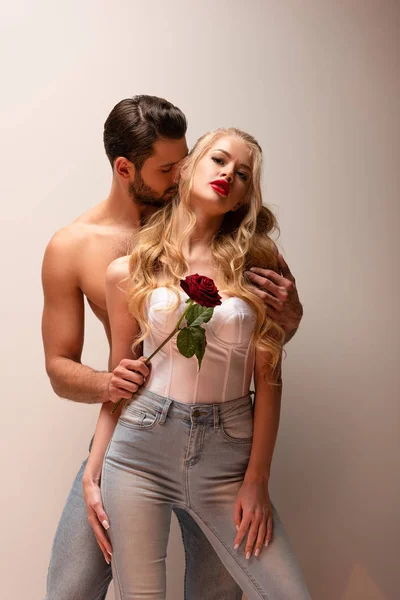 Shirtless man holding rose and touching attractive girl on grey — Stock Photo