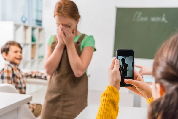 Focus selettivo della studentessa che scatta foto di compagno di classe, concetto di cyberbullismo — Foto stock