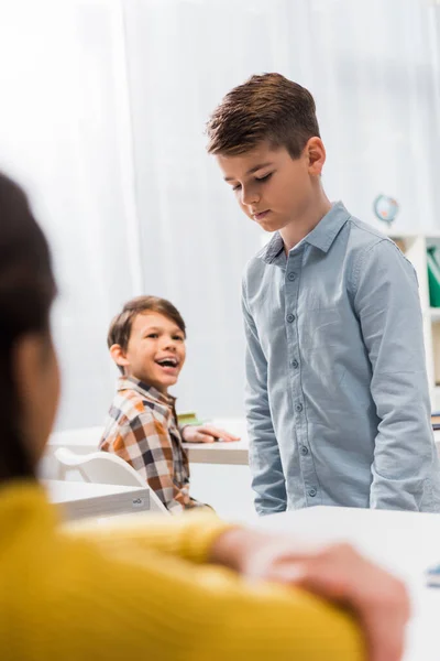 Selective focus of cheerful schoolkids looking at upset schoolboy, bullying concept — Stock Photo