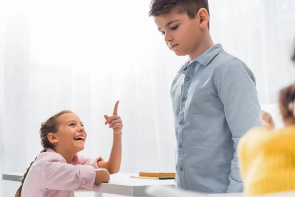 Enfoque selectivo de colegial feliz señalando con el dedo al colegial molesto, concepto de intimidación - foto de stock