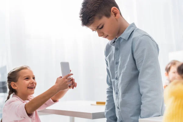 Selective focus of cruel kid smiling while taking photo of bullied classmate, cyberbullying concept — Stock Photo