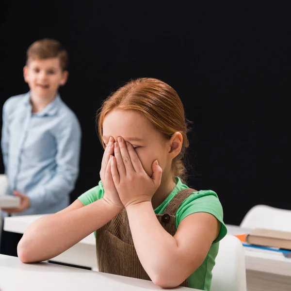 Селективное внимание расстроенного ребенка, плачущего рядом с одноклассником, изолированного от черной, запугивающей концепции — стоковое фото