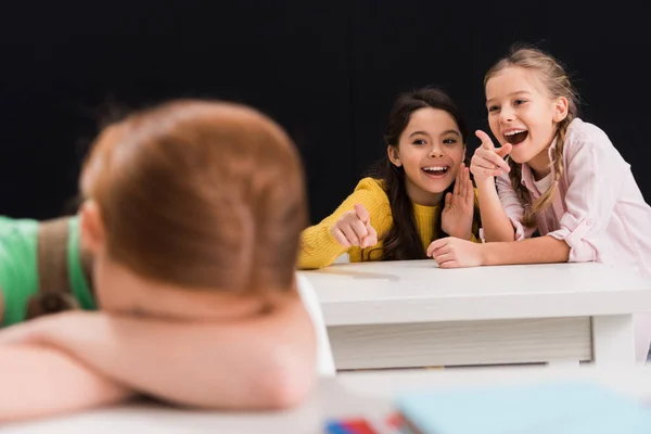 Вибірковий фокус щасливих школярів, які вказують пальцями в однокласниках ізольовані на чорному, знущання концепції — стокове фото