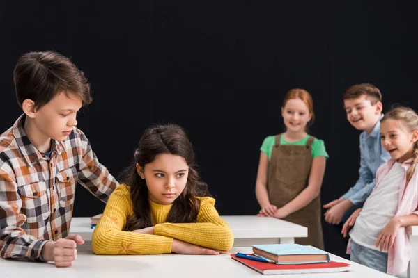 Foyer sélectif de gentil écolier touchant bouleversé écolière près de souriants camarades de classe isolés sur noir, concept d'intimidation — Photo de stock