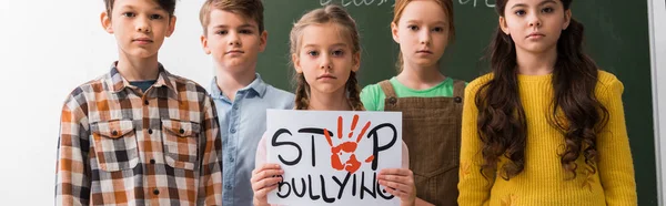Tiro panorâmico de escolares segurando cartaz com lettering stop bullying — Fotografia de Stock
