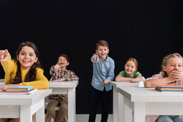 Enfoque selectivo de los escolares señalando con los dedos y riendo aislado en negro, concepto de intimidación — Stock Photo