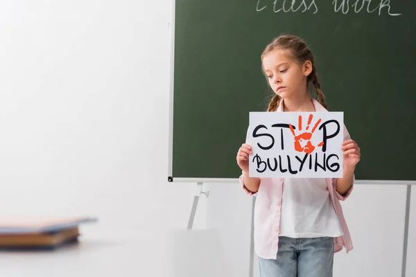 Selective focus of sad schoolgirl holding placard with stop bullying lettering — Stock Photo