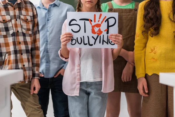 Cropped view of schoolchildren standing near classmate holding placard with stop bullying lettering — Stock Photo