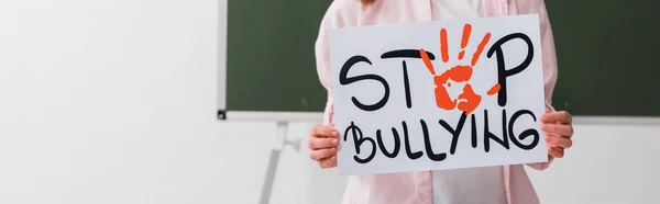 Plano panorámico de colegiala sosteniendo pancarta con letras de stop bullying - foto de stock