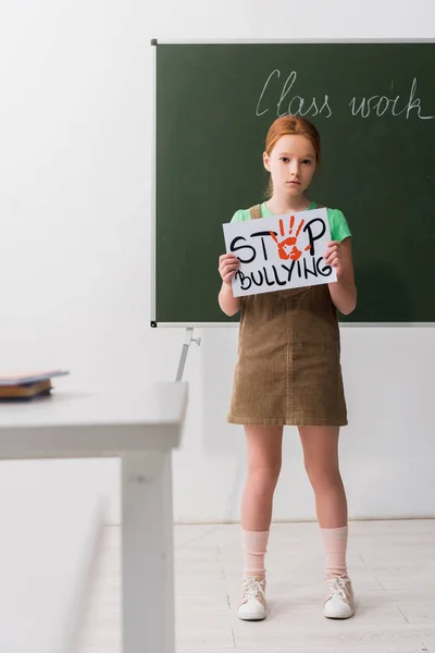 Selective focus of kid holding placard with stop bullying lettering in classroom — Stock Photo