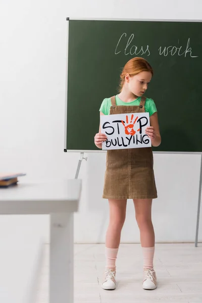 Foyer sélectif de l'écolière mignonne tenant la plaque avec arrêter l'intimidation lettrage — Photo de stock