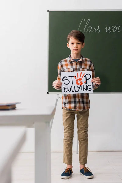 Enfoque selectivo del colegial sosteniendo pancarta con letras de stop bullying - foto de stock
