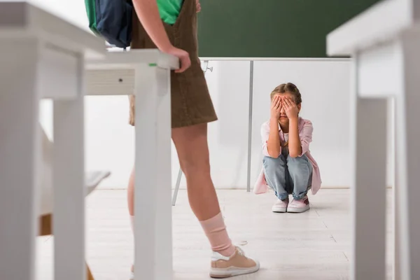 Enfoque selectivo de los escolares de pie cerca de compañero de clase cubriendo la cara mientras llora, concepto de intimidación - foto de stock