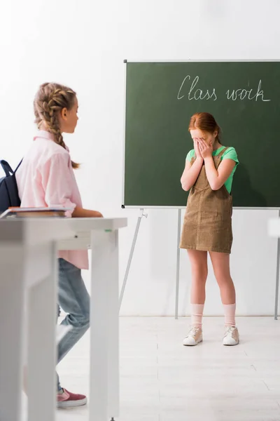 Selective focus of schoolgirl looking at classmate covering face while crying at school, bullying concept — Stock Photo