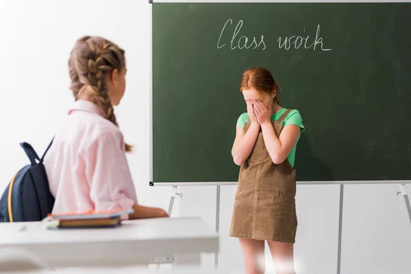 Foco seletivo de colegial cobrindo rosto enquanto chora perto de colega de classe, conceito de bullying — Fotografia de Stock