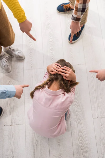 Vista superior de los escolares crueles señalando con los dedos a la colegiala acosada - foto de stock