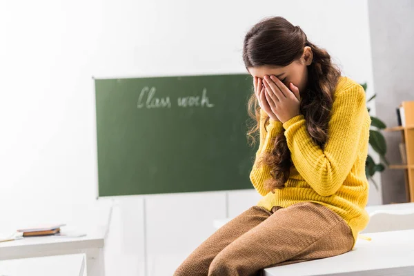 Aufgebrachte und gemobbte Schülerin verdeckt Gesicht, während sie im Klassenzimmer weint — Stockfoto