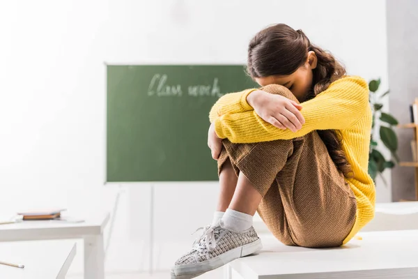 Bullied schoolgirl covering face while crying in classroom — Stock Photo
