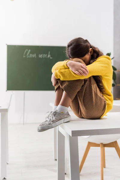 Sad and bullied schoolgirl covering face while crying in classroom — Stock Photo
