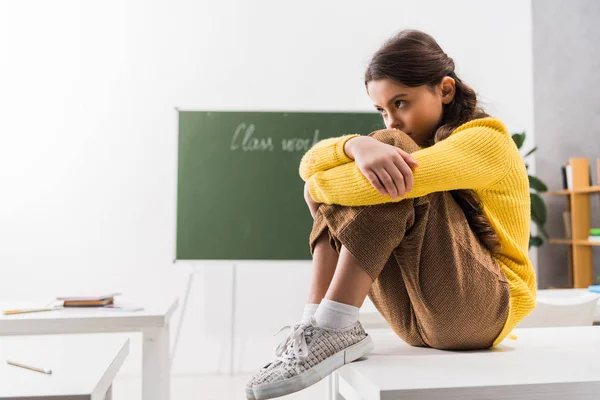 Upset and bullied schoolgirl sitting alone in classroom — Stock Photo