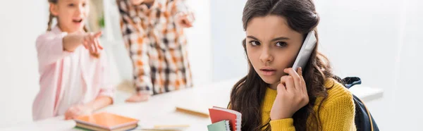 Plano panorámico de niño acosado hablando en el teléfono inteligente cerca de compañeros de clase crueles - foto de stock