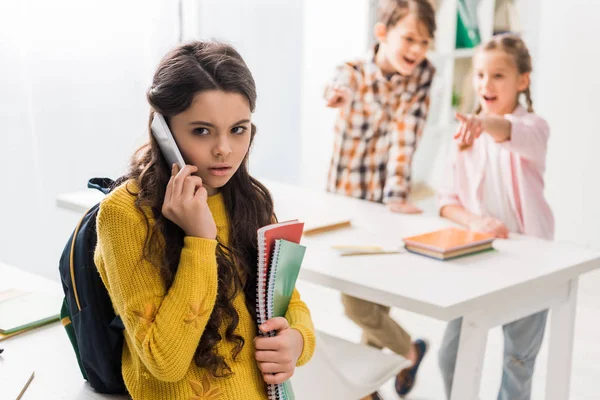 Selective focus of bullied schoolgirl talking on smartphone near cruel classmates — Stock Photo