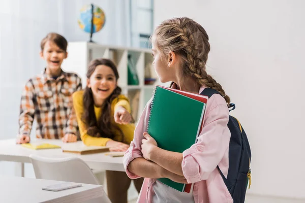 Selective focus of bullied schoolgirl holding notebooks near cruel schoolkids — Stock Photo