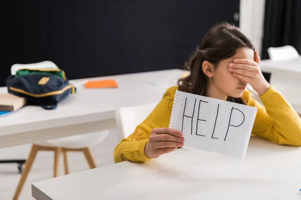 Disgustada colegiala sosteniendo papel con letras de ayuda y cubriendo los ojos, concepto de bullying - foto de stock