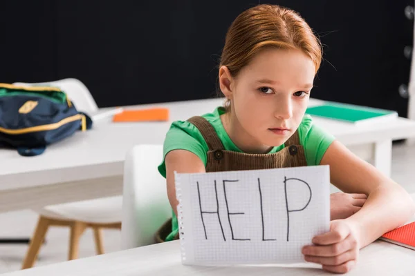 Selective focus of depressed schoolkid holding paper with help lettering, bullying concept — Stock Photo