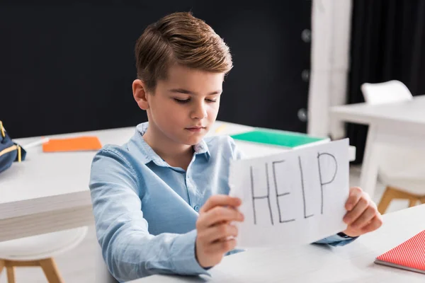 Selective focus of depressed schoolchild holding paper with help lettering, bullying concept — Stock Photo