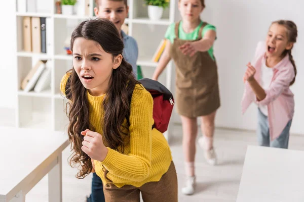 Selective focus of bullied schoolgirl running from cruel classmates, bullying concept — Stock Photo