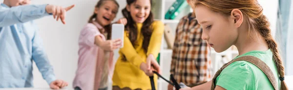 Panoramic shot of schoolkids bullying schoolgirl in classroom — Stock Photo