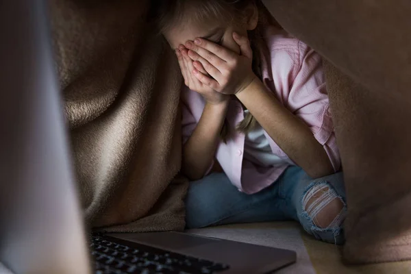 Foyer sélectif de l'enfant frustré couvert de couverture couvrant le visage tout en pleurant près d'un ordinateur portable, concept de cyberintimidation — Photo de stock