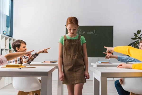 Cruel classmates pointing with fingers at bullied schoolkid in classroom — Stock Photo