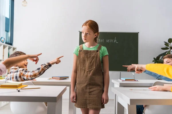 Cruels camarades de classe pointant du doigt l'écolière harcelée dans la salle de classe — Photo de stock