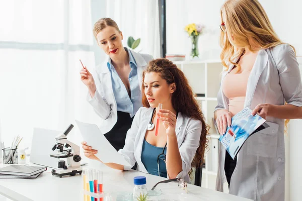 Beautiful and sexy nurses looking at test tube with sample in laboratory — Stock Photo