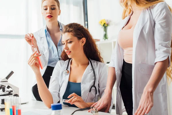 Attractive and sexy nurses looking at test tube with sample in laboratory — Stock Photo