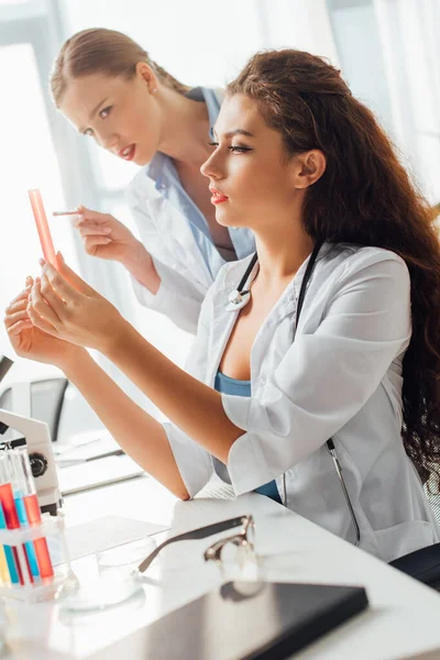 Selective focus of attractive and sexy nurses looking at test tube with liquid — Stock Photo