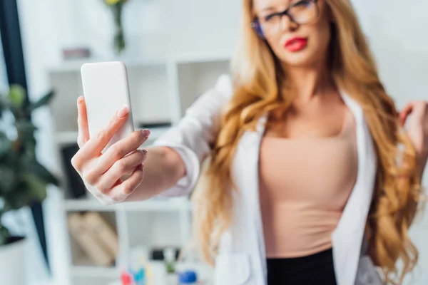 Enfoque selectivo de enfermera sexy en bata blanca tomando selfie en la clínica - foto de stock